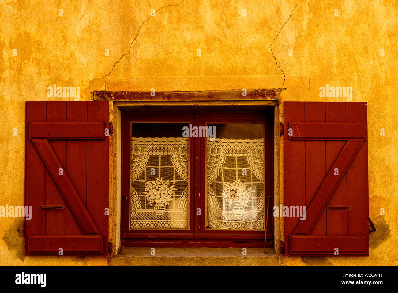 Córcega, Francia. De agosto de 1990. Una ventana en una pared amarilla con cortinas de encaje. Foto: © Simon Grosset. Archivo: Imagen digitalizada de una transparencia original. Foto de stock