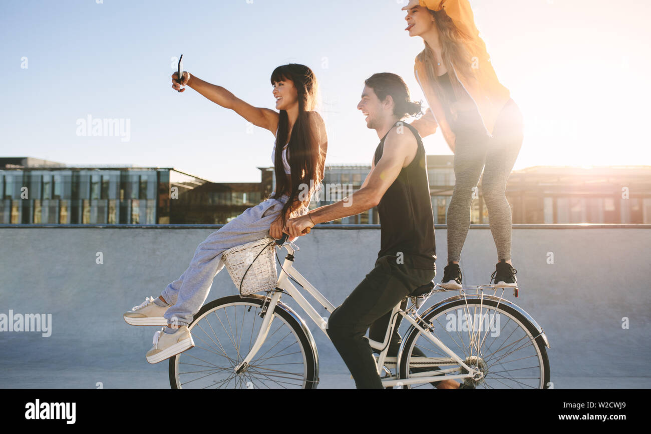 Amigos en bicicleta posando para un selfie. Hombre joven sentado sobre la  bicicleta con amigas en un día soleado Fotografía de stock - Alamy