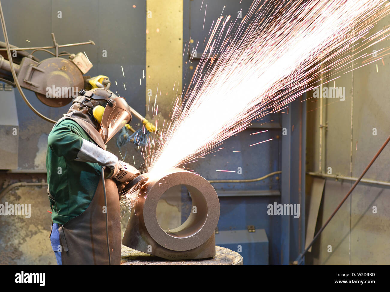 Los trabajadores de equipos de protección en el trabajo de la fundición en un casting con una máquina de moler en el lugar de trabajo Foto de stock