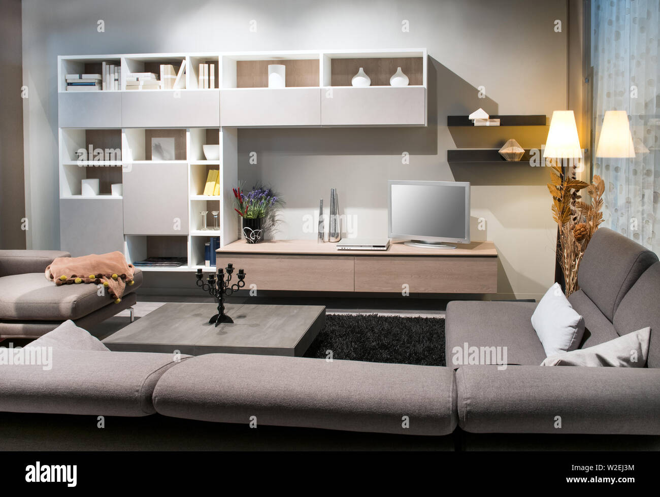 Salón Moderno interior con tapizados cómodos sofás marrones hacia una vitrina y televisión iluminada por abajo y una lámpara de luces Foto de stock