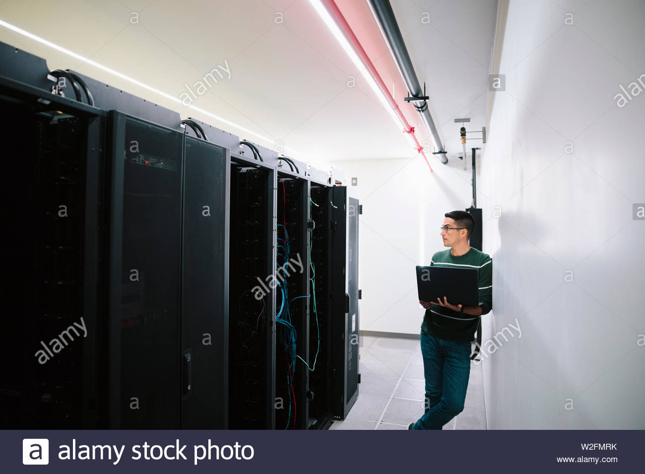 Técnico de ti varón con laptop en la sala de servidores de red Foto de stock