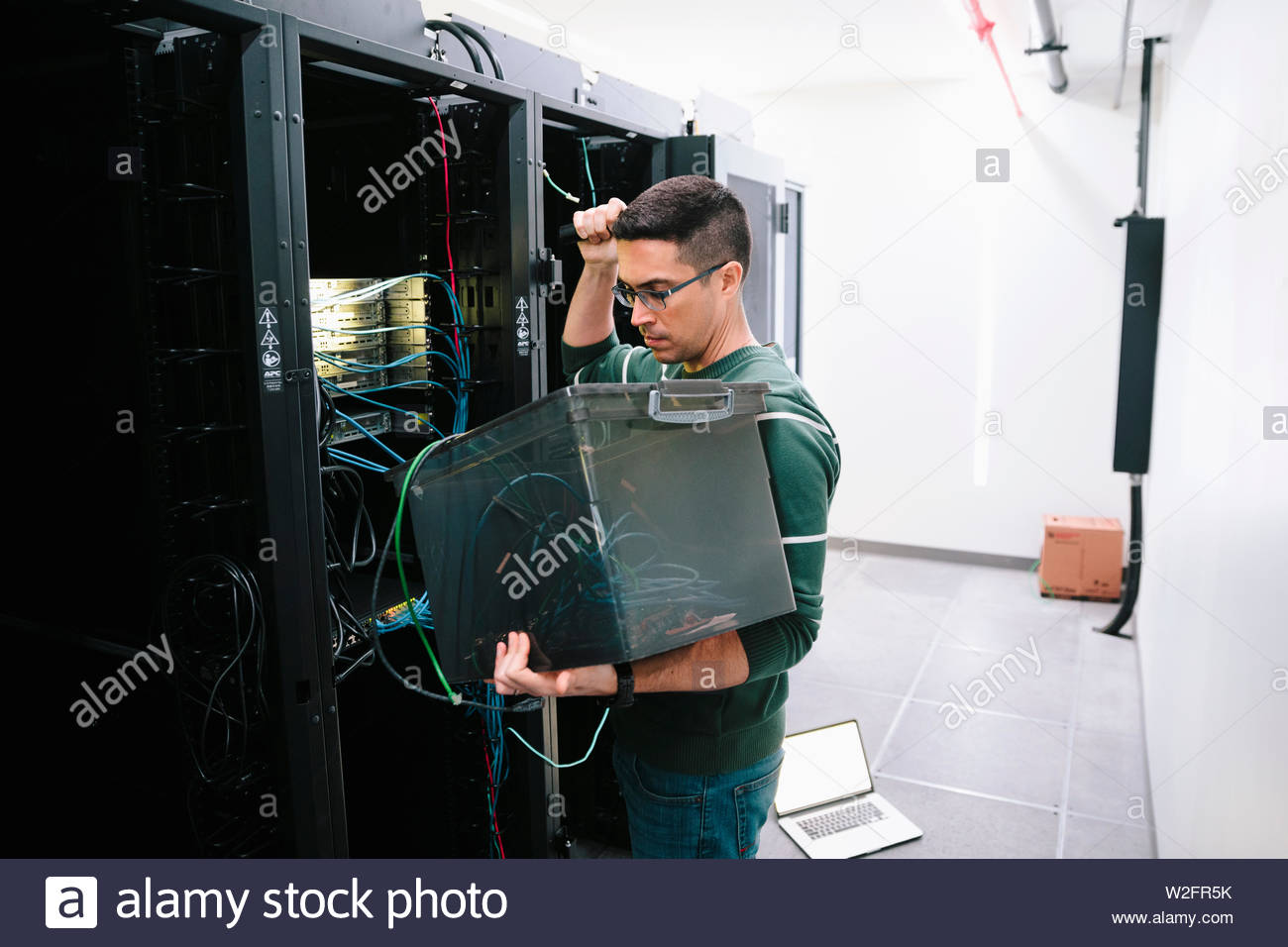 Técnico de ti varón examen del material en la sala de servidores de red Foto de stock
