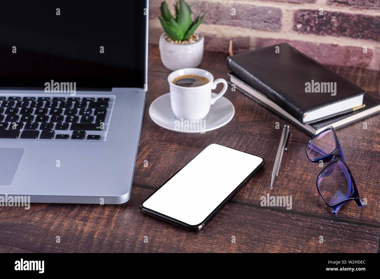Portátil con pantalla en blanco y una taza de café y el bloc de notas y lápiz Libros y teléfonos inteligentes en la mesa de madera. Maqueta de mesa de madera con portátil wi Foto de stock