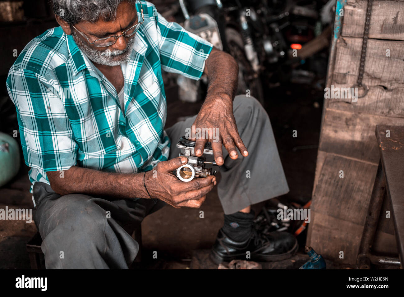 Un mecánico en un pequeño taller en la India, reparación del carburador en una vieja motocicleta. Foto de stock
