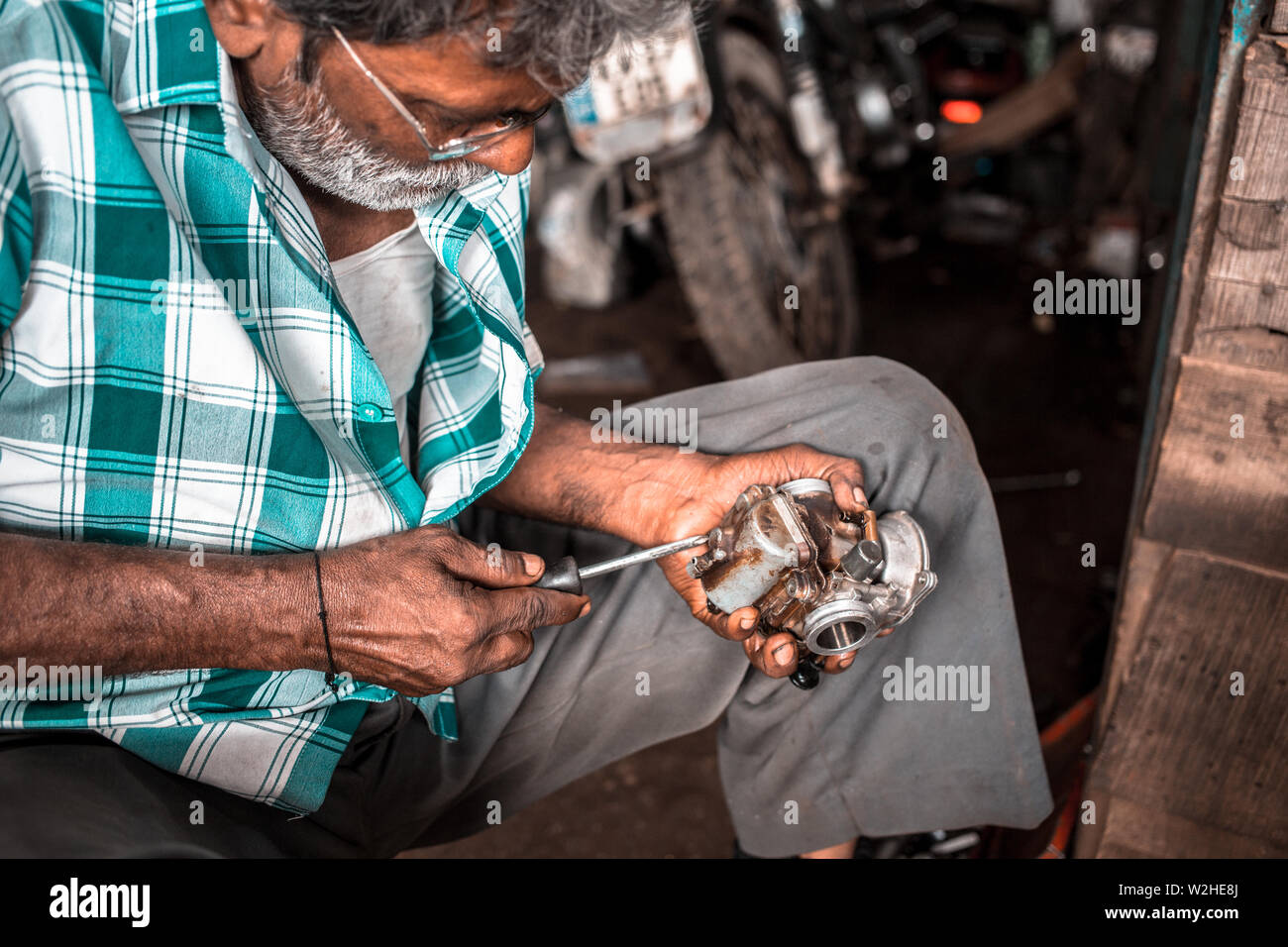 Un mecánico en un pequeño taller en la India, reparación del carburador en una vieja motocicleta. Foto de stock