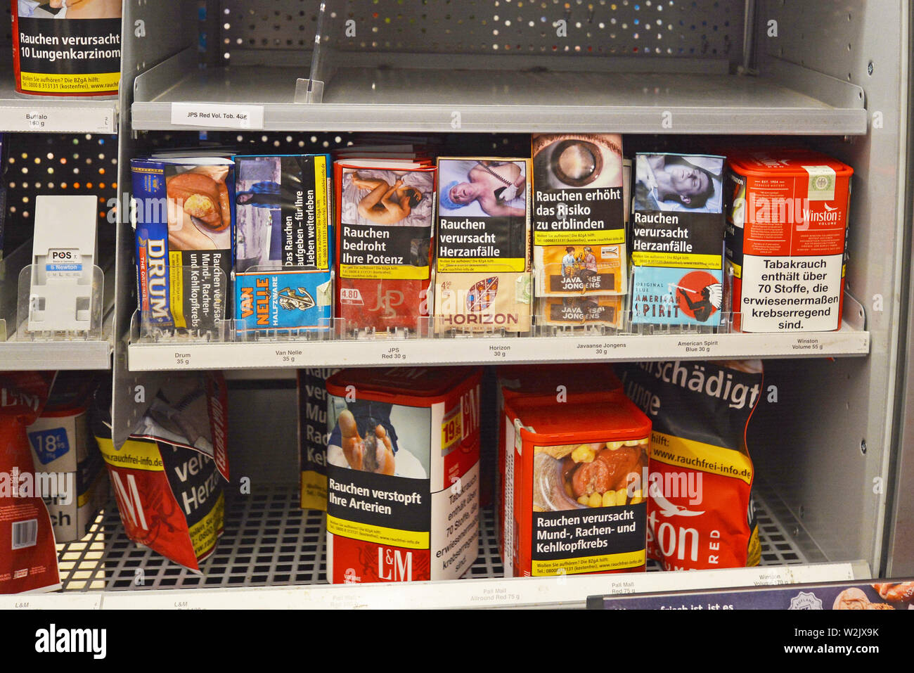 Estantería con los paquetes de tabaco para enrollar cigarrillos con etiquetas de advertencia sobre ellos en supermercado alemán Foto de stock