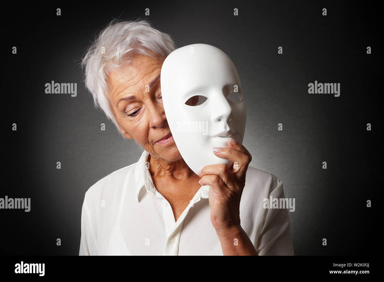 Mujer de edad con cabello blanco ocultando triste rostro detrás de la máscara: la depresión o el concepto de personalidad Foto de stock
