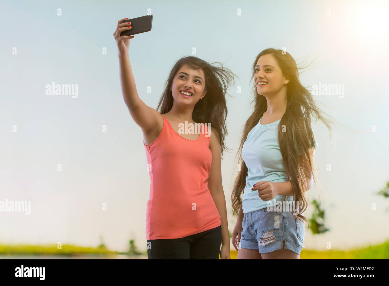 Sonriente joven teniendo un selfie mediante teléfono móvil con un amigo de pie afuera Foto de stock