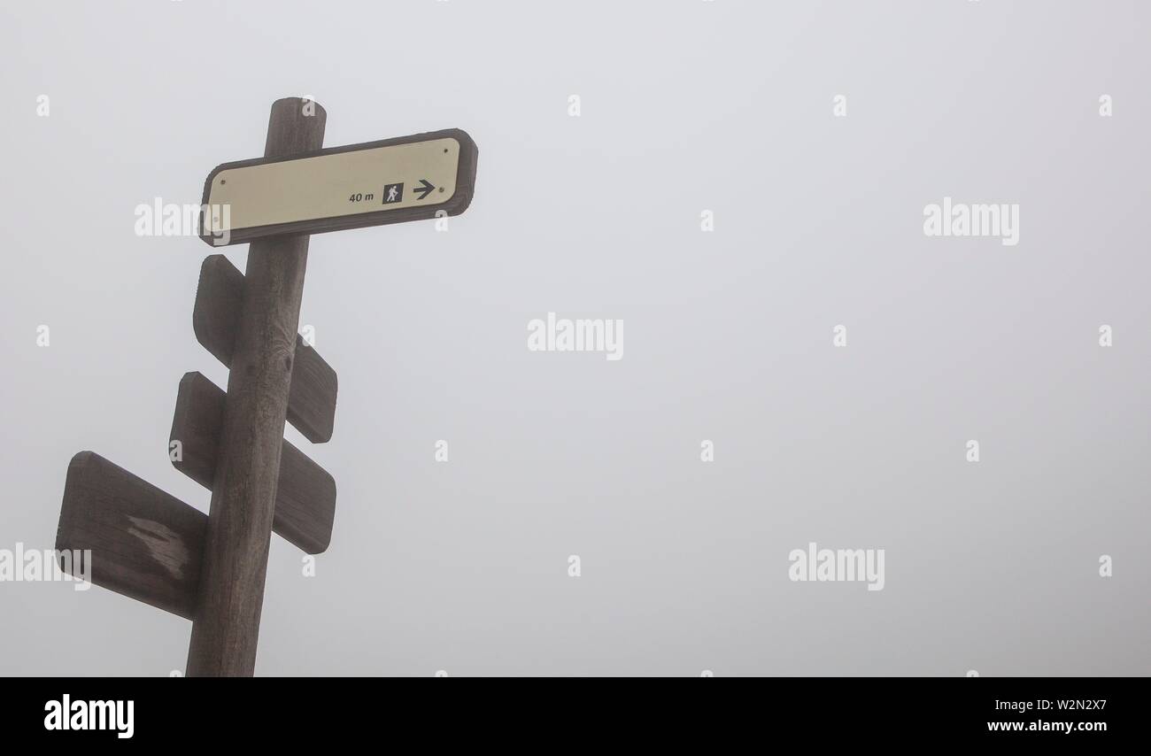 Wet rusty palo de madera con pistas de excursionismo de dirección en una espesa niebla. El Torcal de Antequera. Foto de stock