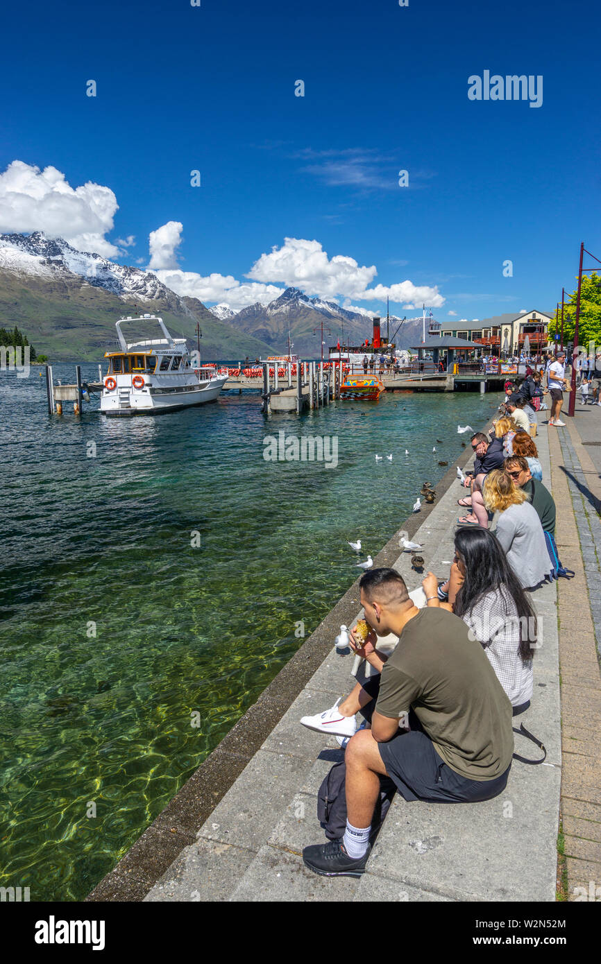 Los turistas sentados en la orilla del lago Wakatipu en Queenstown en día soleado, Isla del Sur, Nueva Zelanda Foto de stock