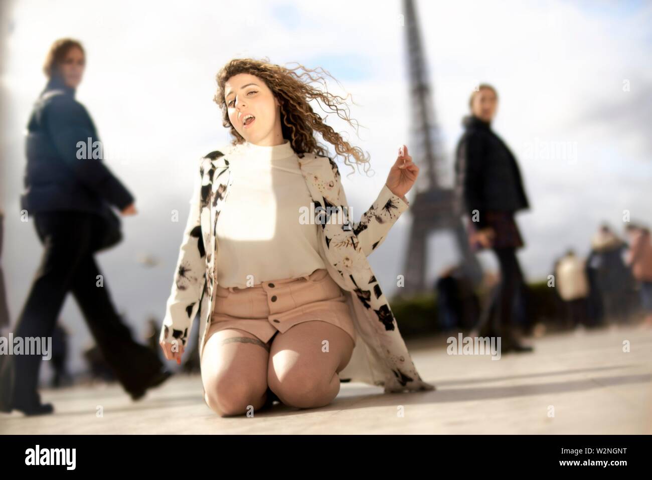 Mujer desenfrenada de rodillas y baile al aire libre en público en la ciudad, junto a la atracción turística Torre Eiffel, siendo observados por los transeúntes, disfrutando de ella, Foto de stock