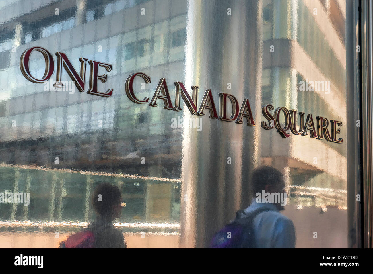 Una Plaza Canadá con placa de entrada de trabajadores a pie de la ciudad se refleja en la superficie de metal brillante fuera de la icónica torre uno Canadá Square en Canary Wharf, London E14 Foto de stock