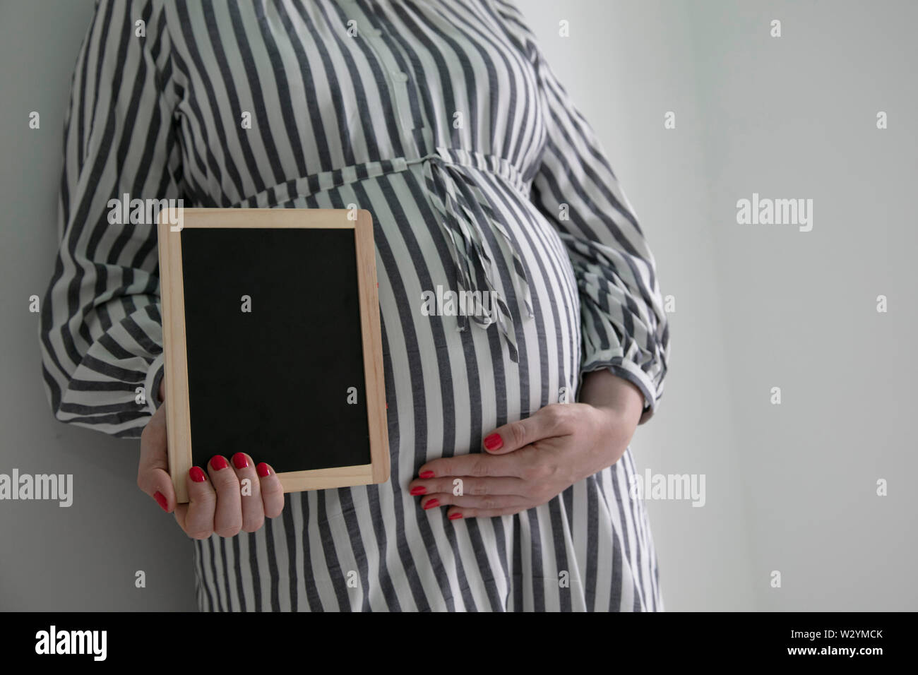 Una mujer embarazada sosteniendo un blak pizarra cerca de ella embarazada vientre Foto de stock