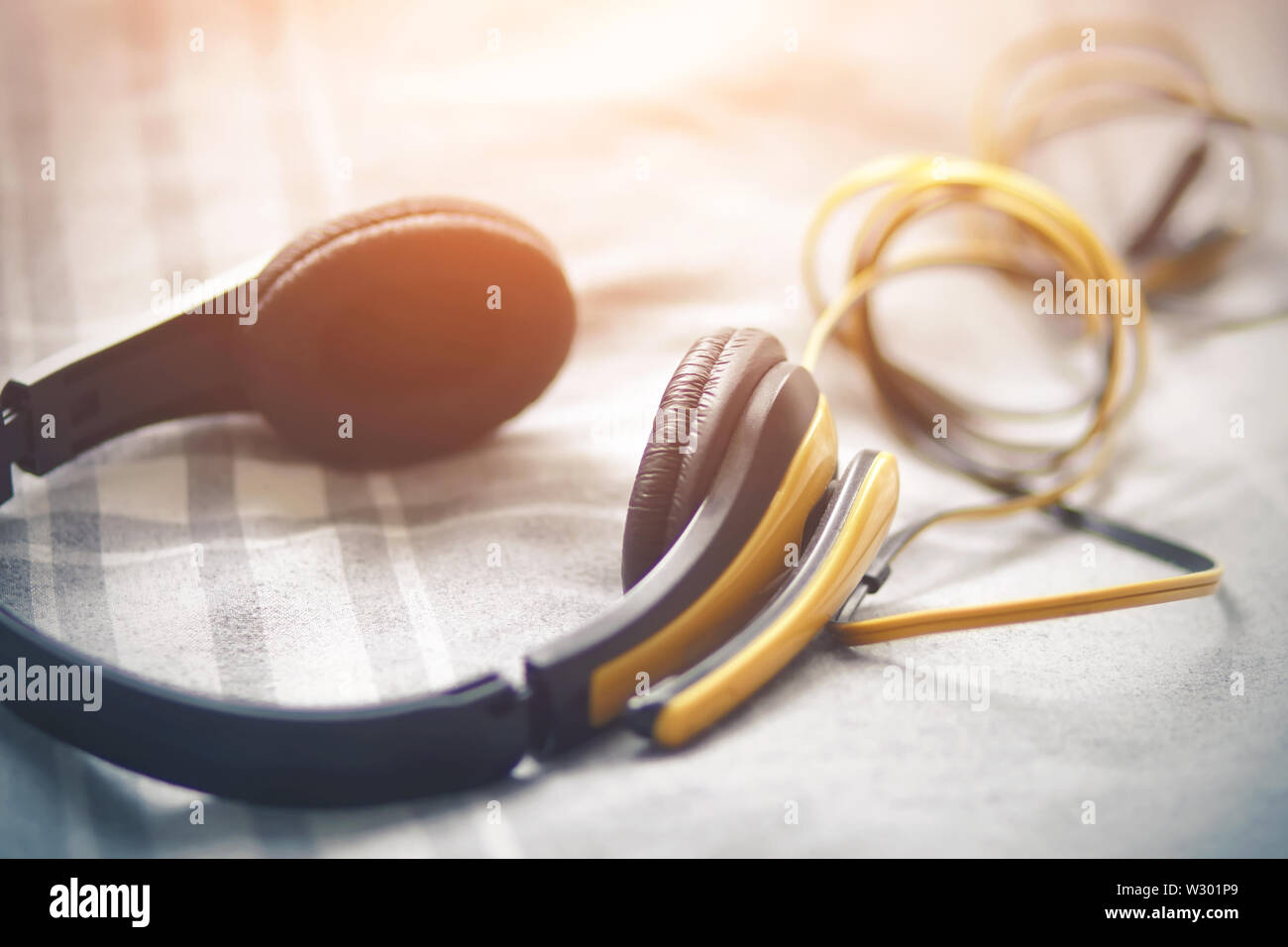 Los grandes auriculares amarillos con un cable largo se encuentran sobre  una manta de lana de cuadros azul suave, iluminada por la luz del sol  brillante. Inspiración y aficiones. Escucha a ple
