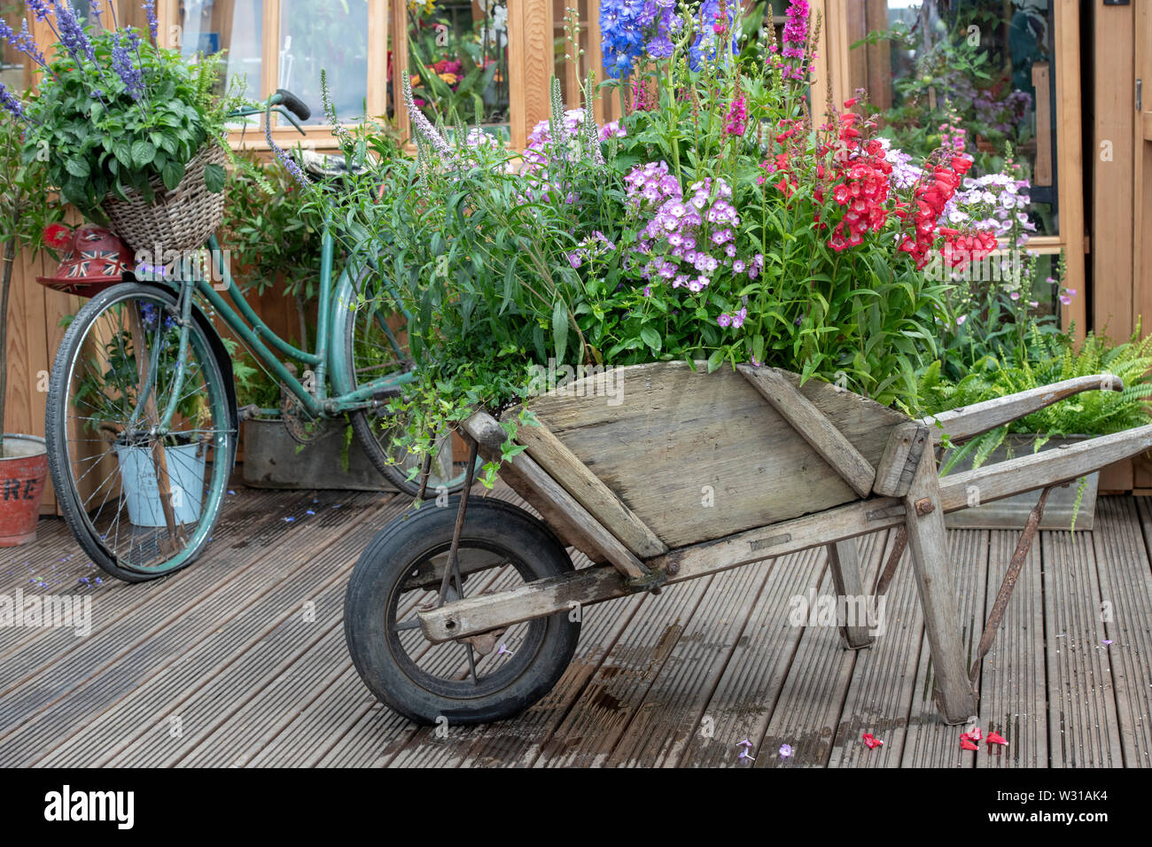 Carretilla de mano vieja y bicicleta en frente de un invernadero en una visualización en RHS Hampton Court Flower Show 2019. Hampton Court, en Surrey, Inglaterra Foto de stock