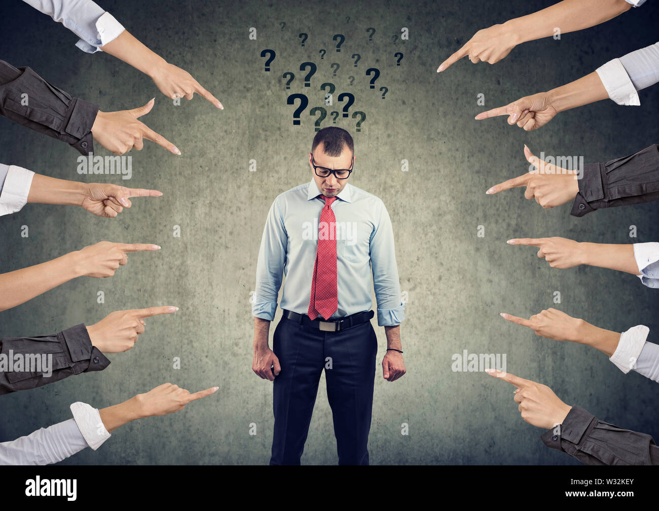 Concepto de acusación. Triste con preguntas mirando hacia abajo con muchos dedos apuntando a él Foto de stock