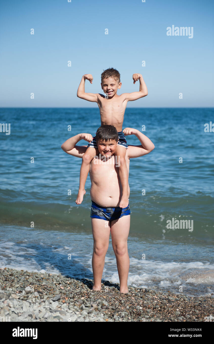 Feliz deporte activo chico sentado en Fat Kid hombros mostrando fuertes  músculos en verano mar sunny beach Fotografía de stock - Alamy