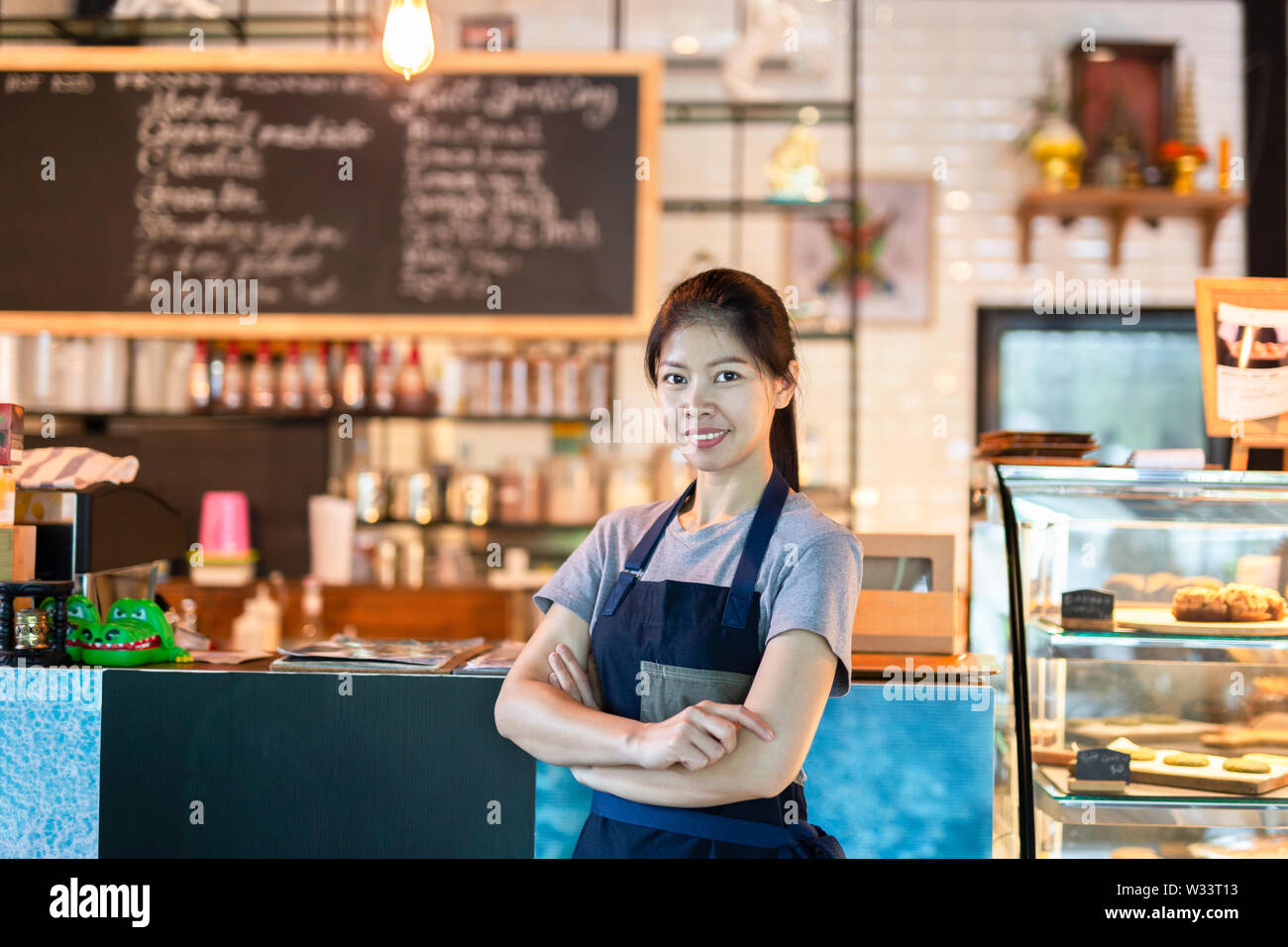 Asian barista mujer de pie con una sonrisa en la cafetería. Foto de stock