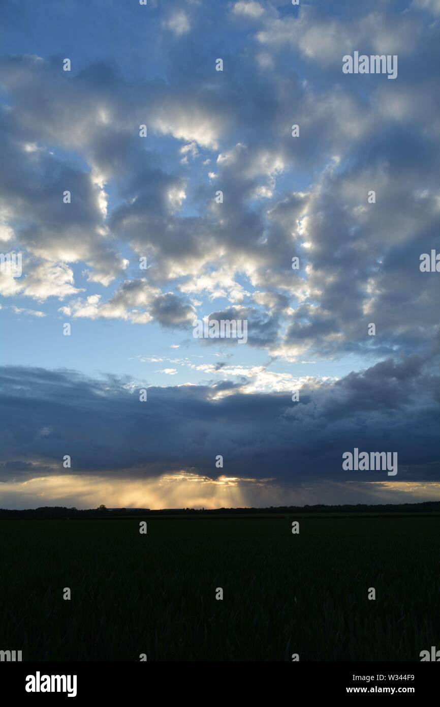 Puesta de sol detrás de las nubes mixtas con rayos de luz mostrando debajo de un banco de nubes. Foto de stock