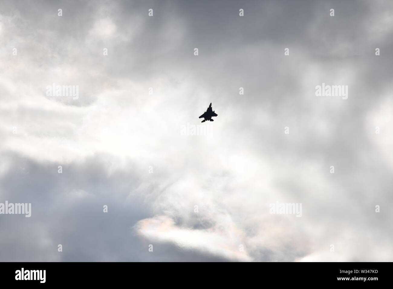 F 15 jet fighter en la distancia subiendo en un gris oscuro cielo nublado con sol casi abstracto patrones de fondo. Foto de stock