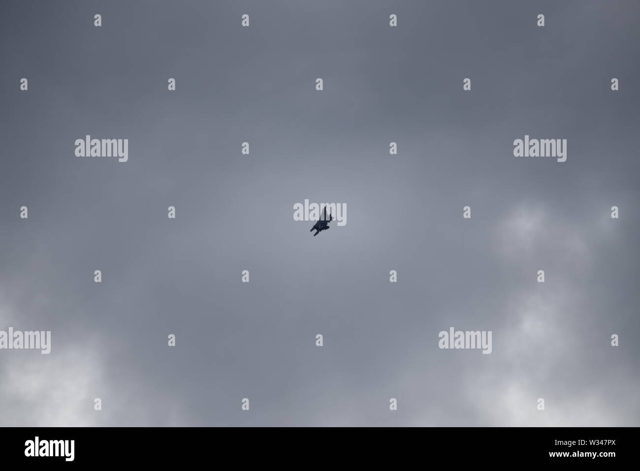 F 15 jet fighter en la distancia subiendo en un gris oscuro cielo nublado con sol casi abstracto patrones de fondo. Foto de stock