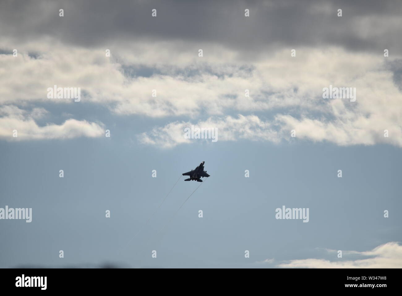 F 15 jet fighter en la distancia subiendo en un gris oscuro cielo nublado con sol casi abstracto patrones de fondo. Foto de stock