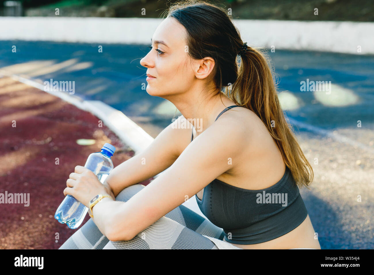 Mujer joven con una botella de agua después de correr afuera en Lisabone. Ella lleva una luz superior gris y leggings de deportes Foto de stock