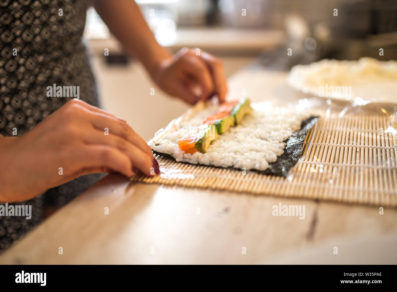 Una mujer preparando y rollos de sushi casero. Formando el sushi. Vista de proceso de preparar sushi de laminación. Foto de stock