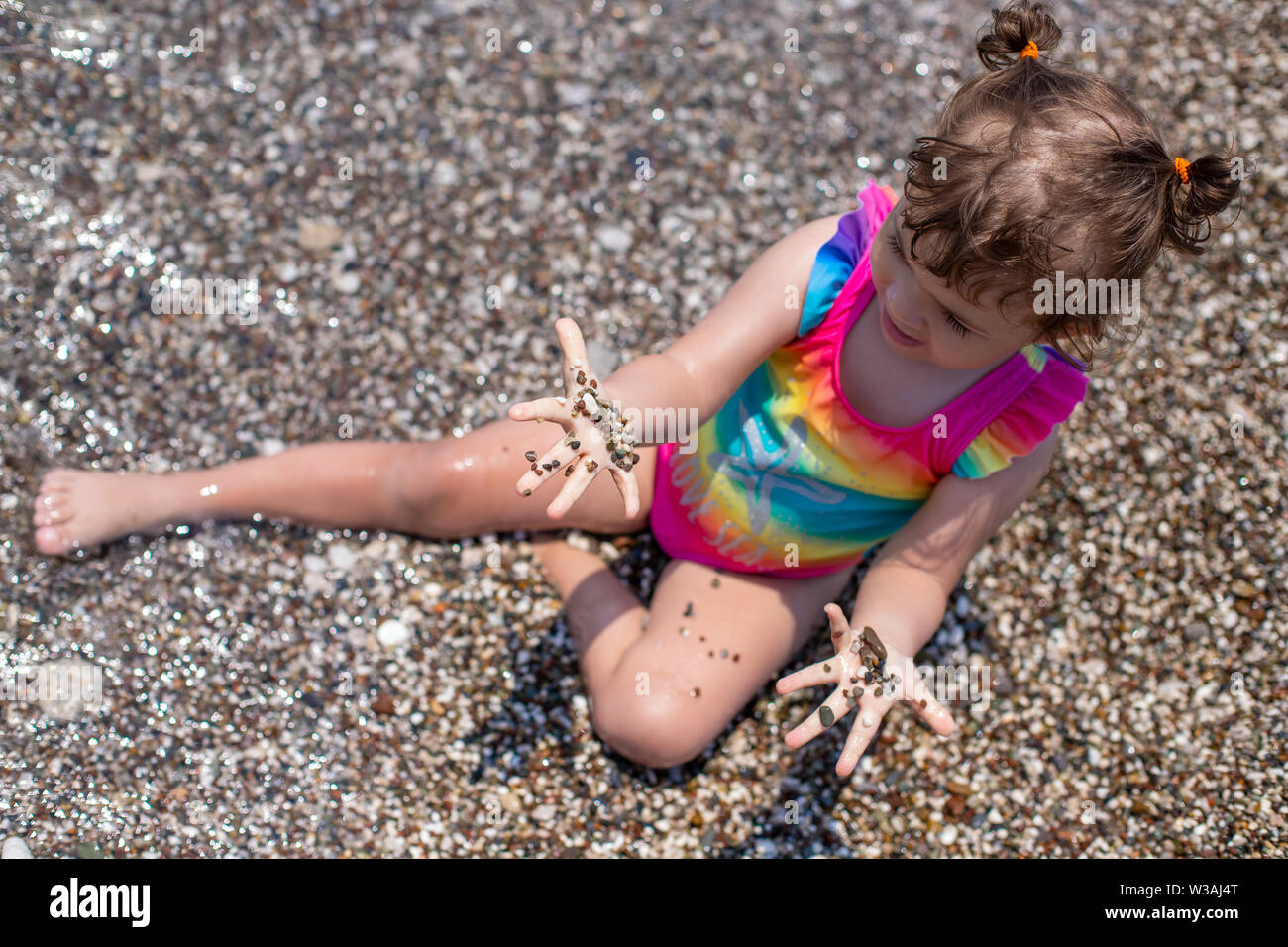 Una niña juega en una playa de guijarros. El desarrollo de las habilidades de motricidad fina. Grandes granos de arena en la playa Foto de stock