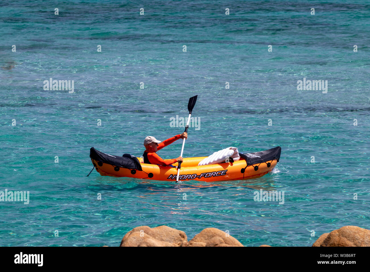 Alghero, Italia - 06.16.2019: el hombre una naranja en palas de kayak de mar, bote de goma. Captura de luz de verano. Foto de stock