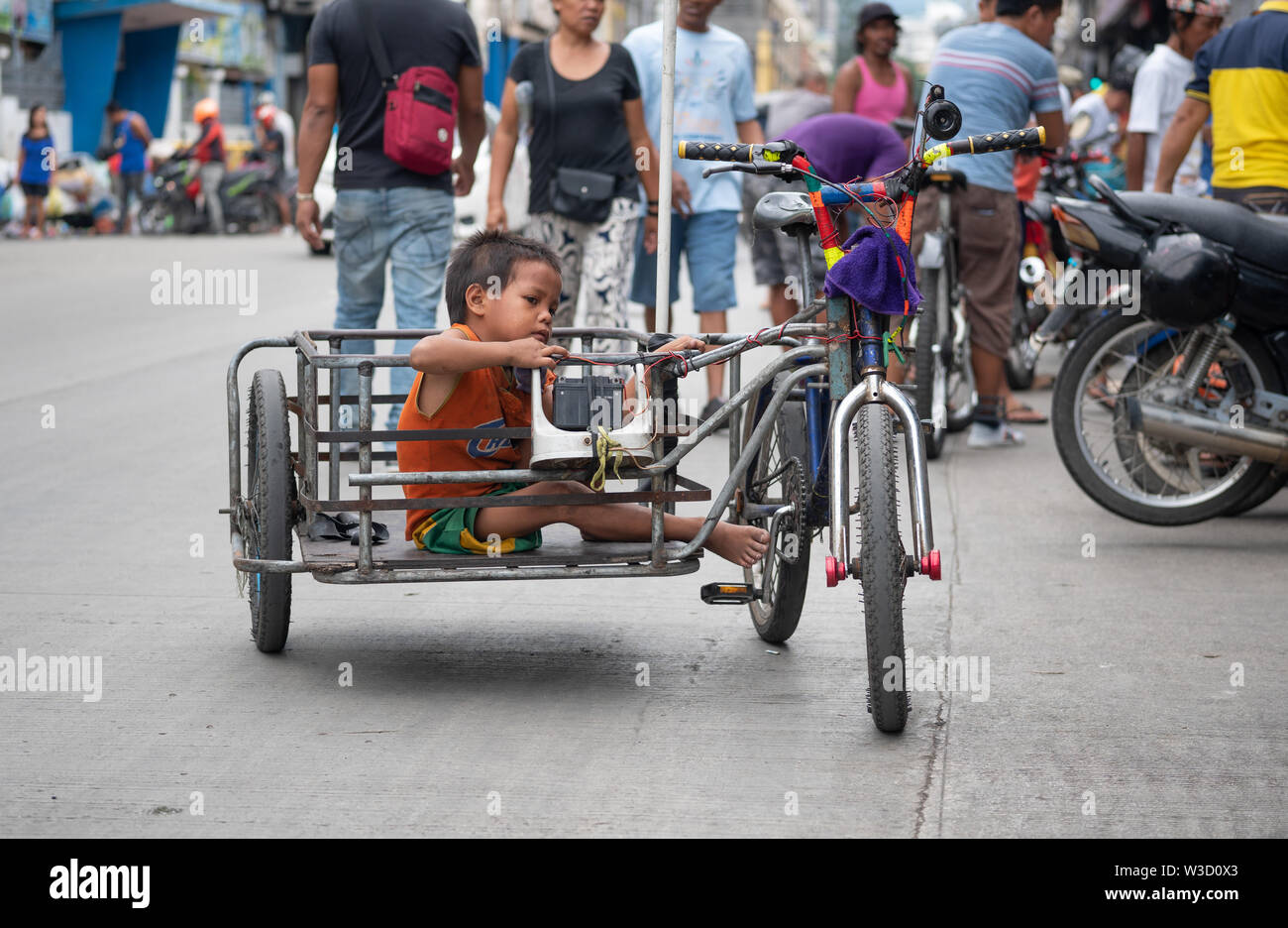 Un niño se sienta en un carro acoplado a una bicicleta.El artilugio es conocido como un Tricicad en Filipinas Foto de stock