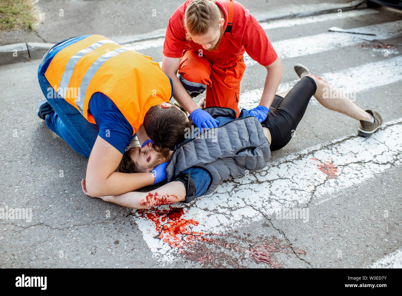 Medic con conductor de coches de aplicar los primeros auxilios a los heridos hombre tumbado en el cruce peatonal después del accidente en carretera Foto de stock