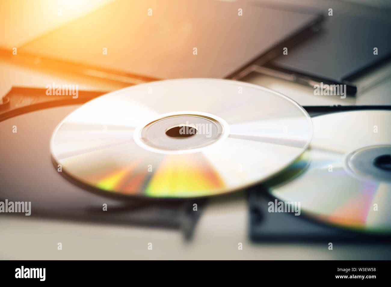 Dos nuevos discos compactos se encuentran junto a las cajas negras de los discos, y está iluminado por la luz del sol, desde el cual los discos brillan en diferentes col Foto de stock