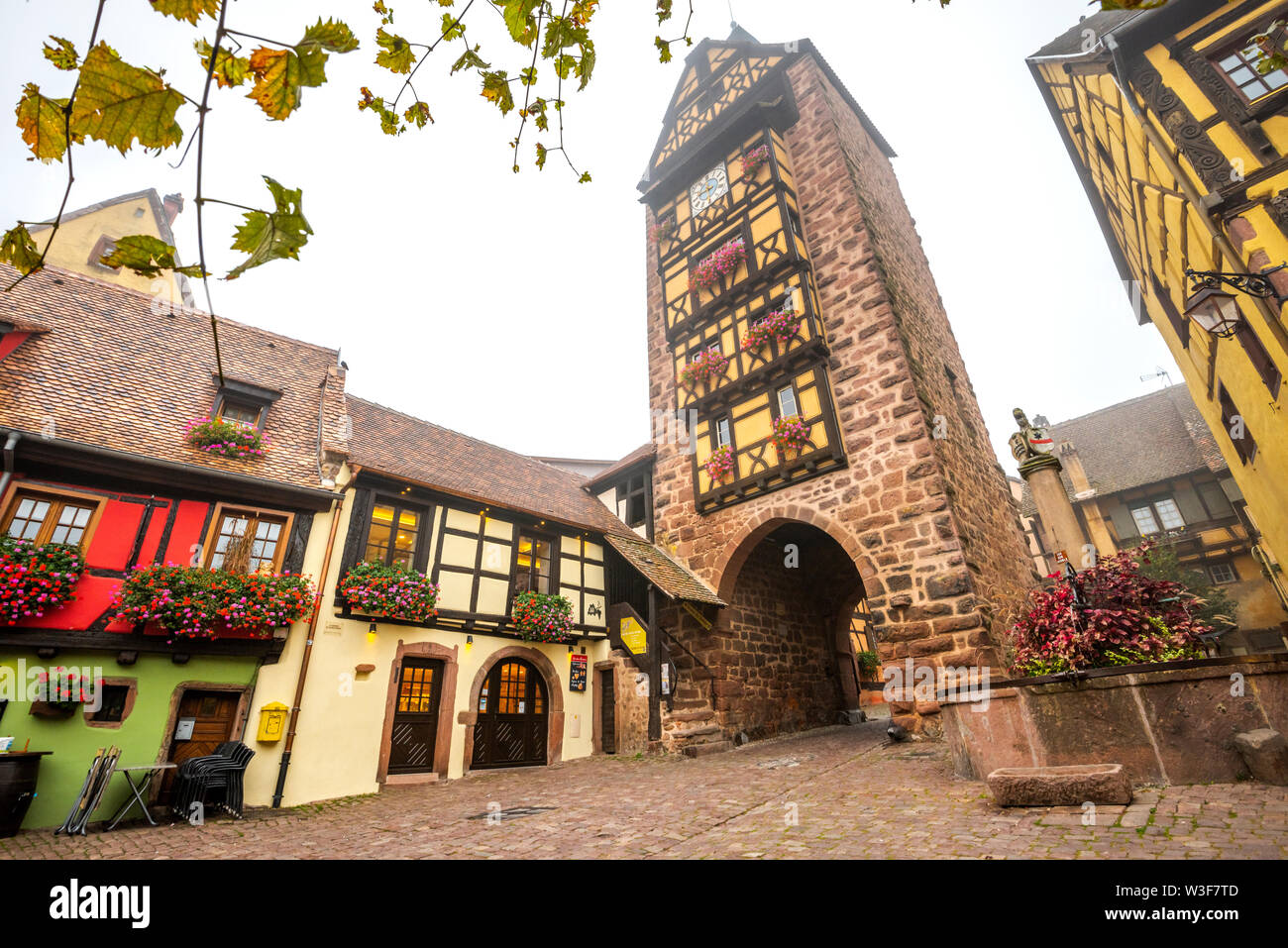 Antigua puerta de la ciudad de la aldea con timberwork Riquewihr, Ruta del Vino de Alsacia, Francia, la histórica torre Dolder y bien adornados de flores Foto de stock