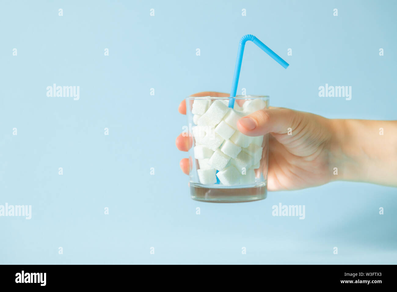 Excesivo consumo de azúcar concepto - la mano que sujeta el cristal con cubos de azúcar Foto de stock