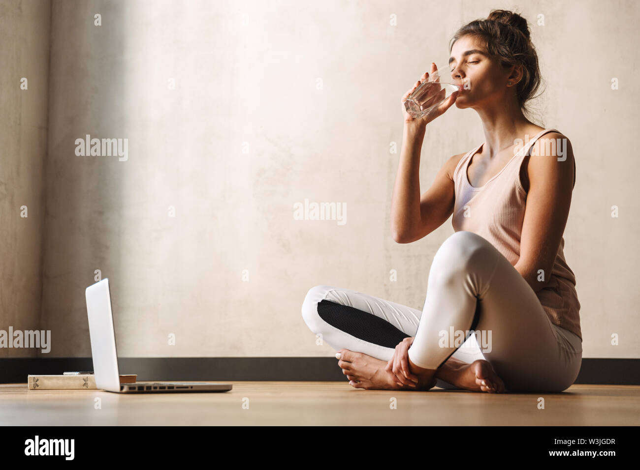 Foto de joven mujer bonita en ropa deportiva agua potable y sentado en el  piso mientras hace ejercicios de yoga en casa Fotografía de stock - Alamy