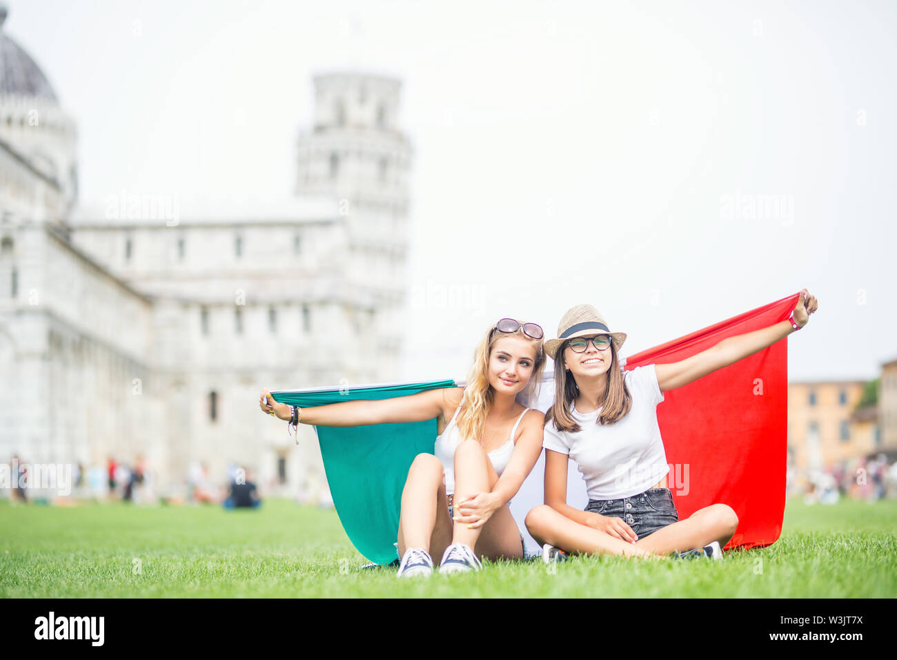 Las niñas adolescentes jóvenes viajeros con bandera italiana antes de la histórica torre en la ciudad de Pisa, Italia. Foto de stock