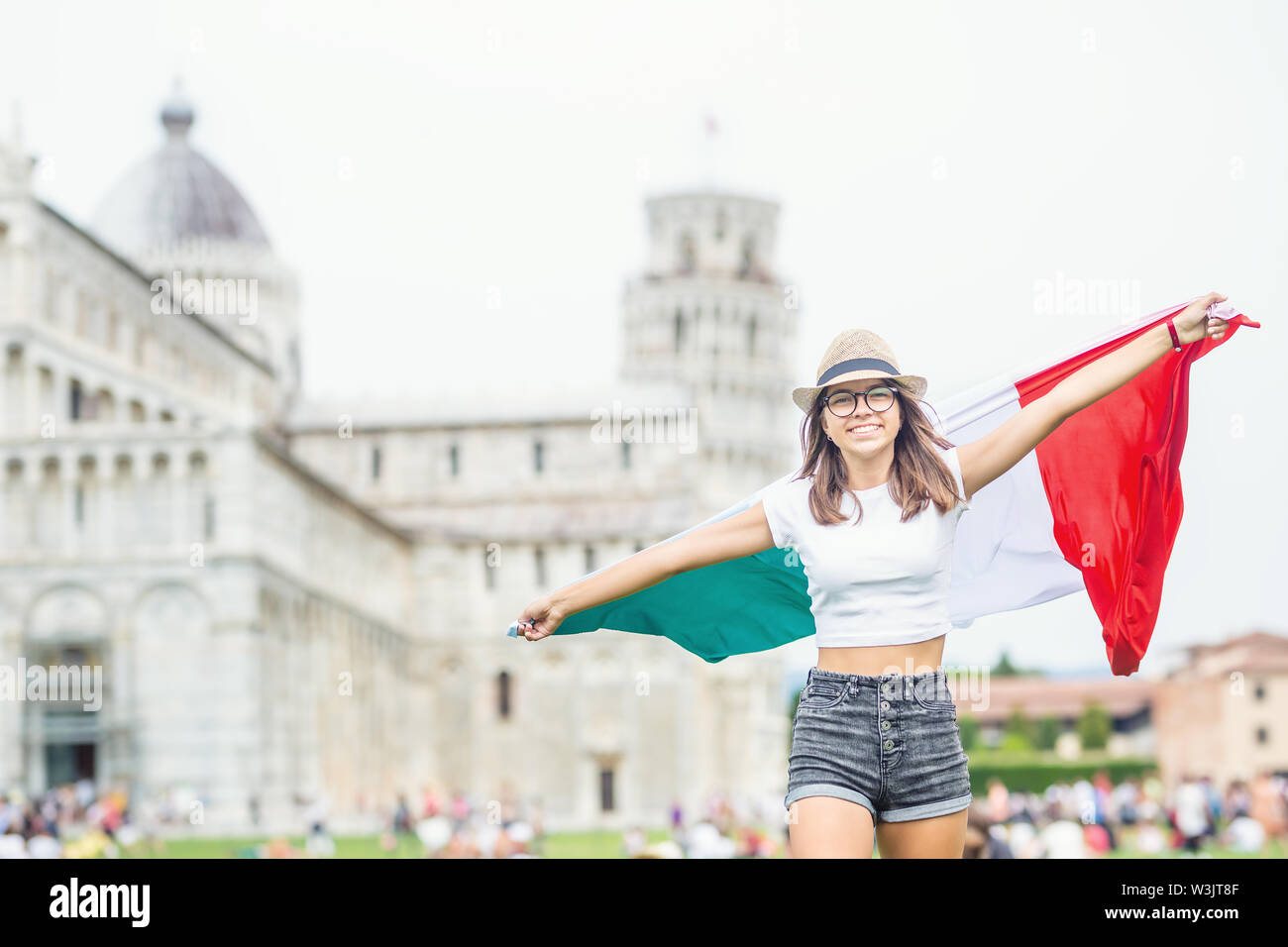 Muchacha adolescente joven viajero con bandera italiana antes de la histórica torre en la ciudad de Pisa, Italia. Foto de stock
