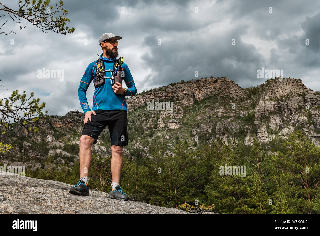 Corredor masculino de pie sobre una roca en las montañas. Atleta corre en  las montañas entre las rocas. Hombre en Azul Jersey y pantalón negro afuera  de formación Fotografía de stock -