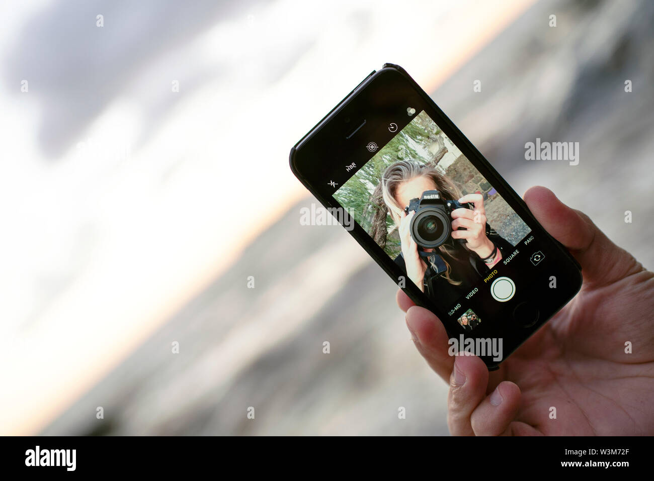 Fotógrafo femenina teniendo un auto-retrato/ selfie mientras un hombre sujetando el smartphone. Fotografía del smartphone, iphoneography viajes/ estilo de vida al aire libre Foto de stock