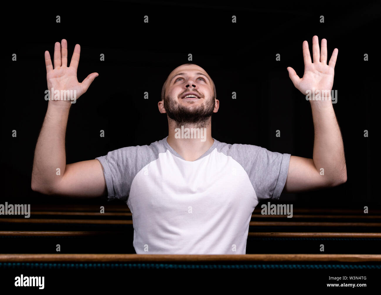 Un hombre cristiano con la camisa blanca está sentado con las manos  levantadas y orando con corazón humilde en la iglesia Fotografía de stock -  Alamy