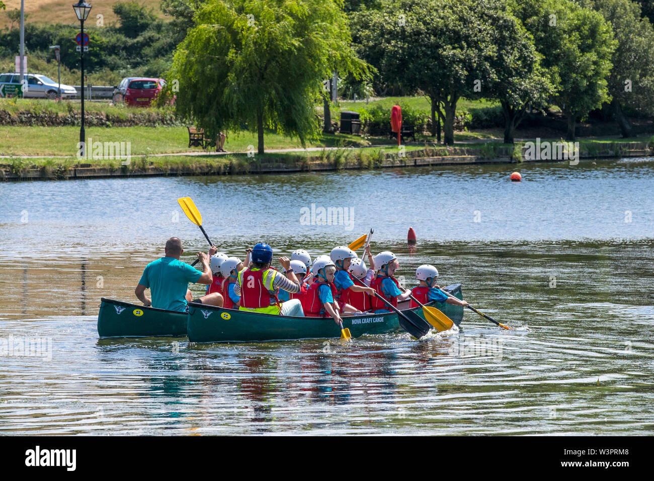 Los alumnos de la escuela primaria de actividad de ocio al aire libre disfrutando de una lección como se divierten canotaje en el lago con botes, Jardines Trenance en Newquay en Cornualles. Foto de stock