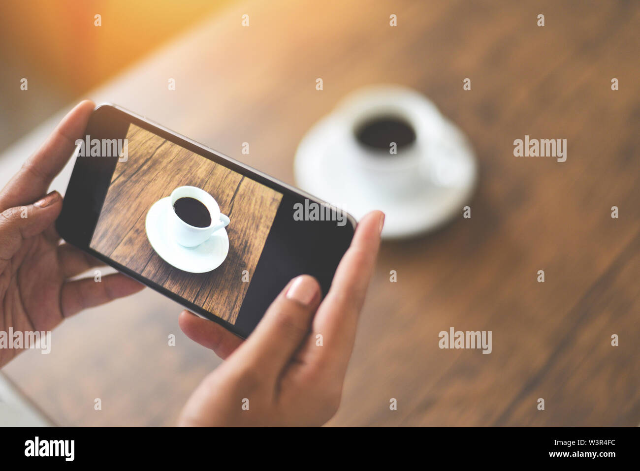 Tomar fotos con la cámara del smartphone de la de café para usar tecnología post cargar archivo en línea en Internet / Cierre de mujer mano sujetando el teléfono móvil