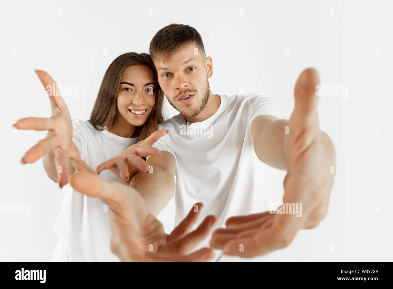 Hermosa pareja joven retrato de estudio aislado en blanco de fondo. La expresión facial, las emociones humanas, el concepto de publicidad. Copyspace. Mujer y hombre de pie tirando manos a la cámara. Foto de stock