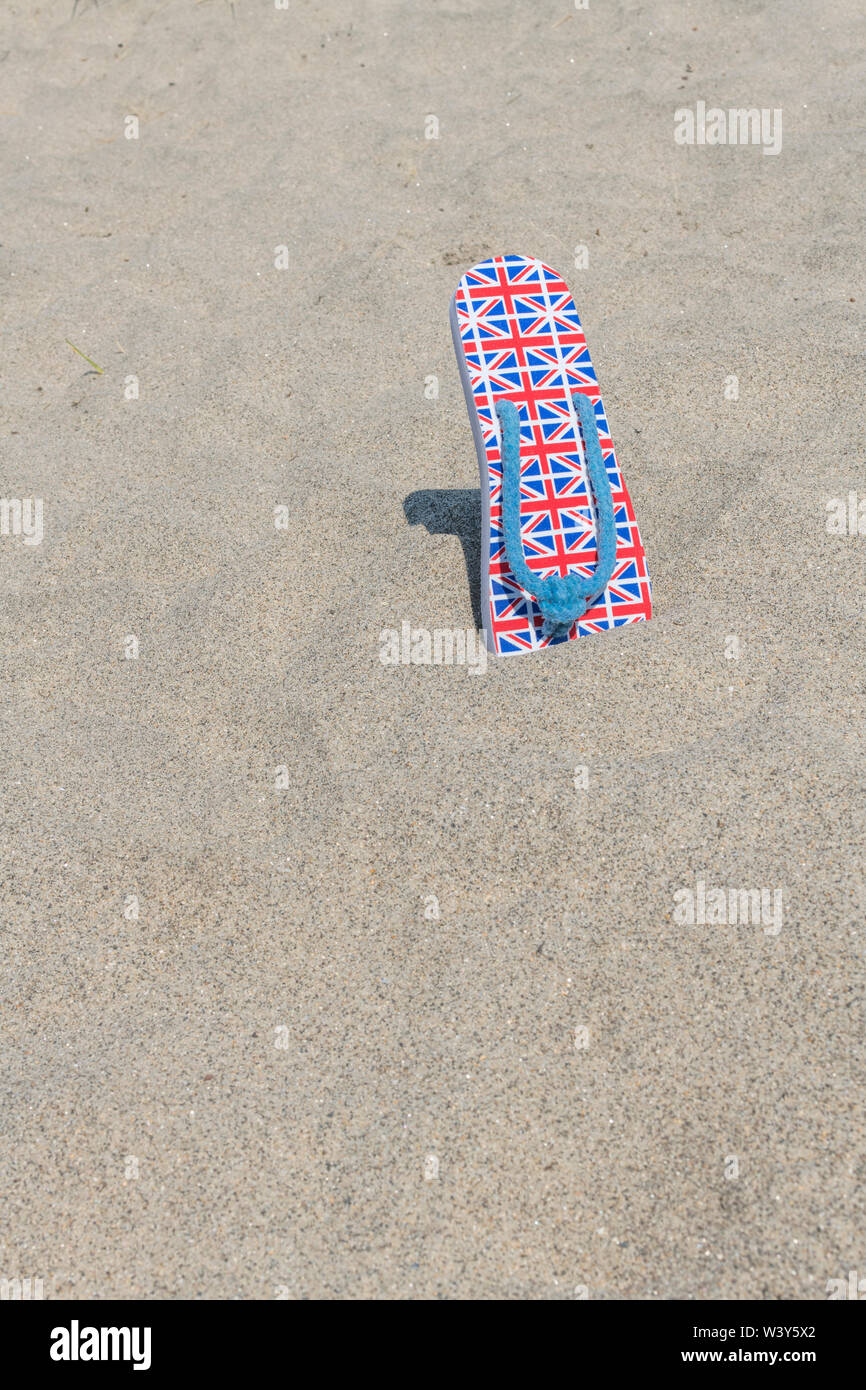 Bandera GB / Flip-flops Union Jack en la playa de arena - para 2021 Reino Unido staycation, vacaciones en casa, staycation Cornwall, vacaciones junto al mar, calzado flip-flop. Foto de stock