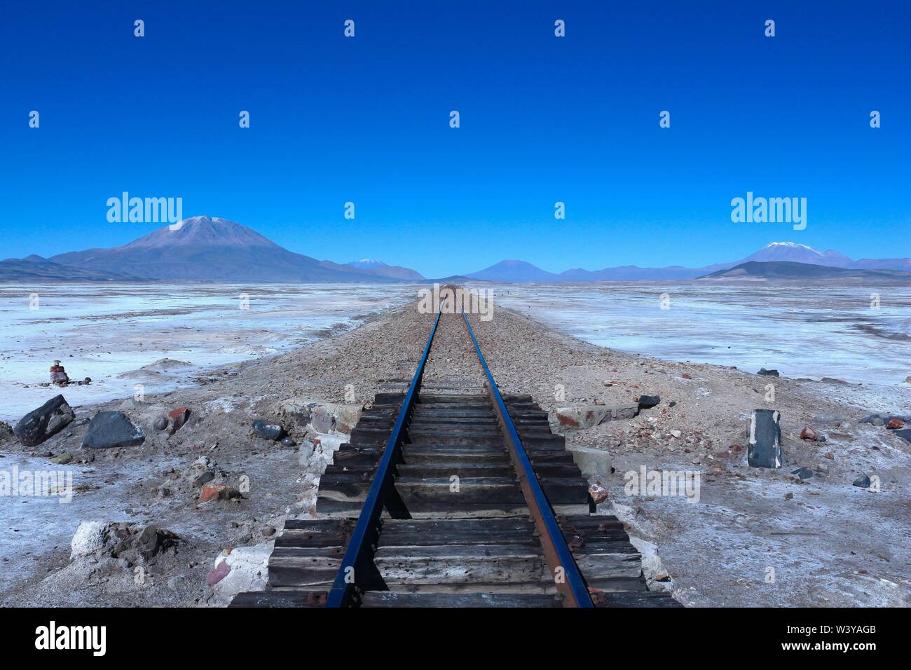 Vía del tren al infinito con volcanes en la espalda, el Salar de Uyuni, Bolivia Foto de stock