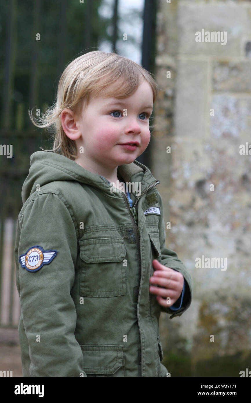 Little Boy (2/3 años), vistiendo un abrigo color caqui y sonriente y disfrutando corriendo alrededor del exterior: Mottisfont, Hampshire, Reino Unido. Modelo liberado Foto de stock
