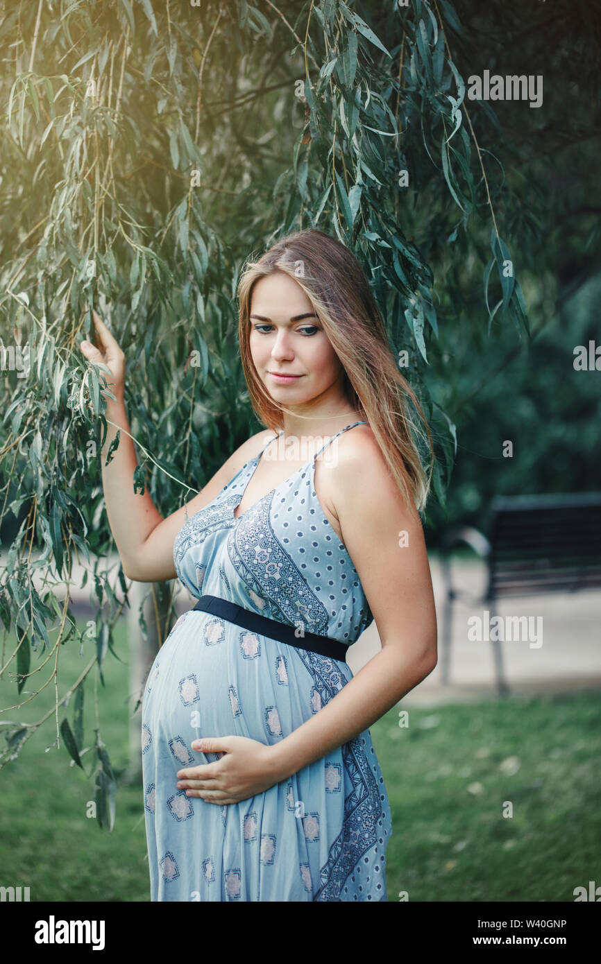 Feliz saludables durante el embarazo y la maternidad. Retrato de mujer caucásica joven embarazada vestidos de largo vestido azul posando en el parque afuera. Hermosa pensive fe Fotografía stock - Alamy