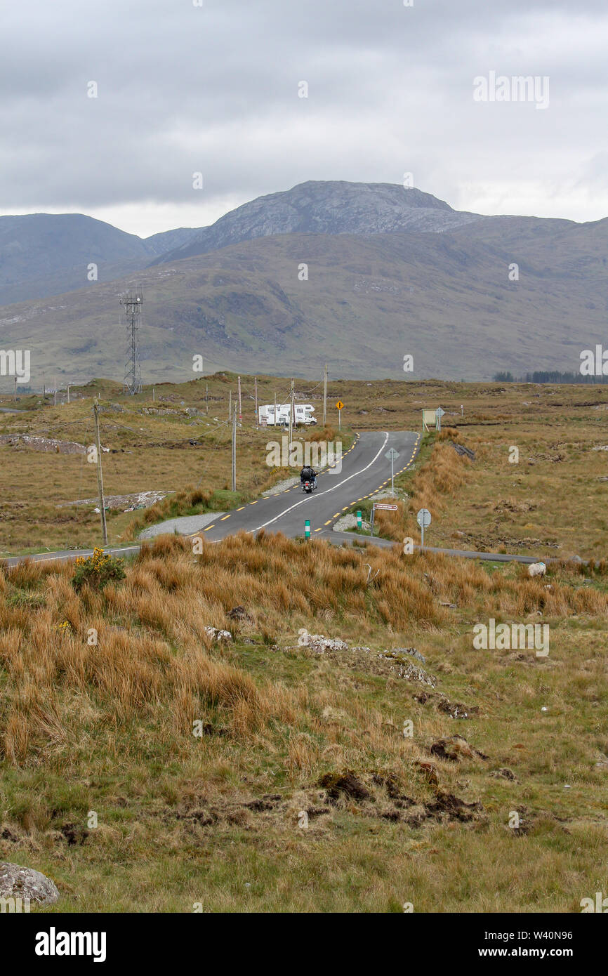 Abrir camino a través de bog tierras en el oeste de Irlanda con un motociclista y autocaravana en una carretera rural hacia Connemara, en el Condado de Galway. Foto de stock
