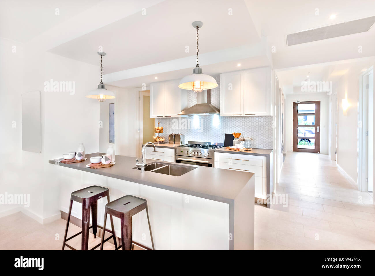 Moderna cocina interior en el día con una manera para ir a una puerta exterior en el piso de baldosa, hay sillas de plástico cerca del contador Foto de stock